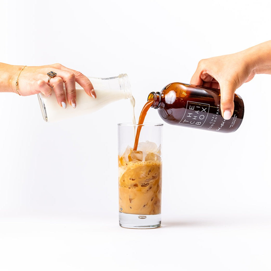 Chai concentrate being pour into an iced glass with milk. 